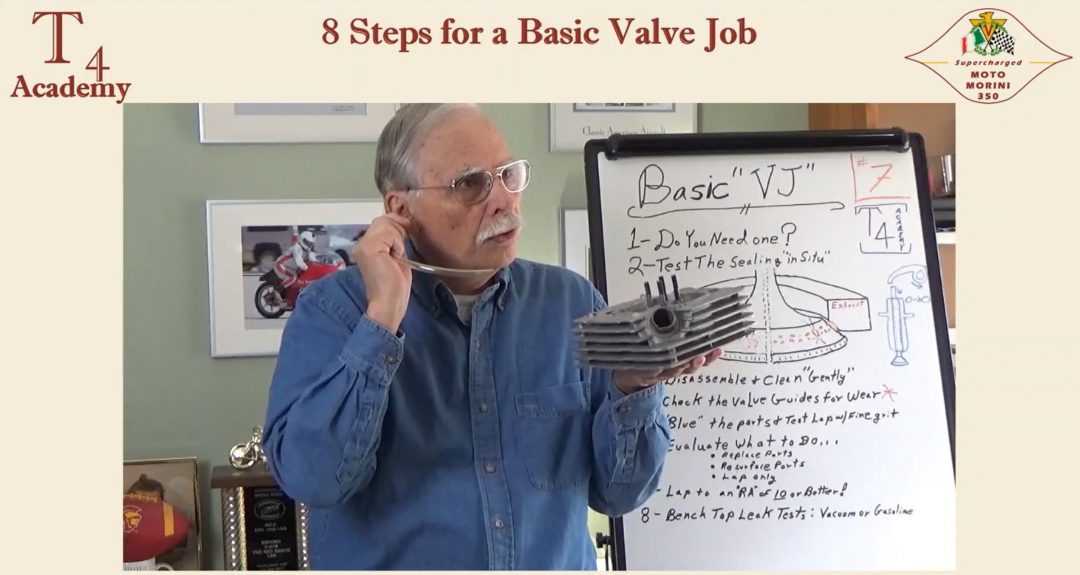 Smitty has a plastic tube in his ear while holding a cylinder head, mimicking the sound you would hear with a leaky valve.